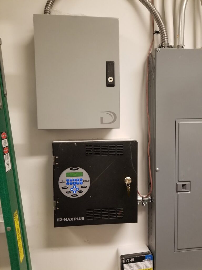 Two commercial control panels, including an EZ-MAX PLUS unit, mounted next to an electrical panel by KS Retail Solutions in Victoria, TX
