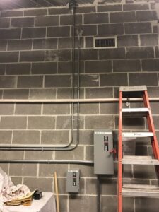Commercial electrical conduits and disconnect switches installed on a cinder block wall by Lighten Up Electric, LLC in Cranston, RI.