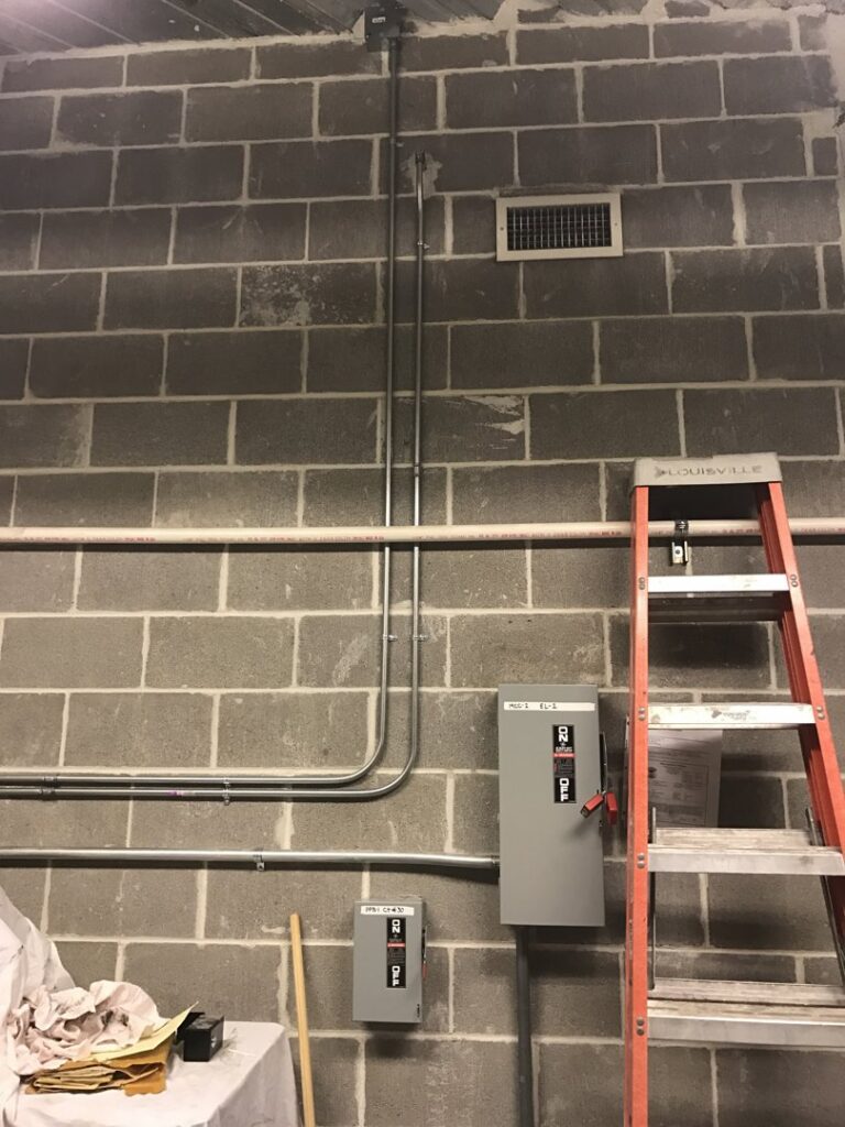 Commercial electrical conduits and disconnect switches installed on a cinder block wall by Lighten Up Electric, LLC in Cranston, RI.