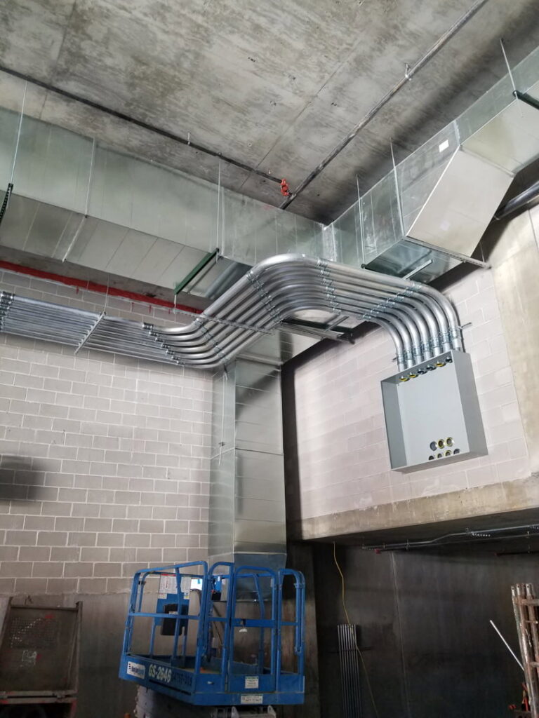 Electrical conduits installed along a wall and ceiling in a commercial space, with a scissor lift nearby, by Bottom To The Top Electric LLC in Lakewood, CO.