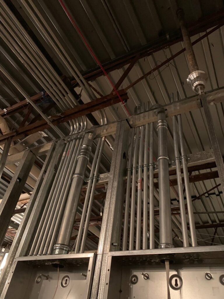 Commercial electrical conduits and junction boxes installed along a ceiling and wall, showcasing work by Volta Electrical LLC in Plano, TX.