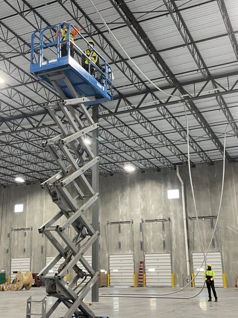 Electricians on a scissor lift installing electrical conduit in a commercial building for Cardinal Electric in Sayreville, NJ