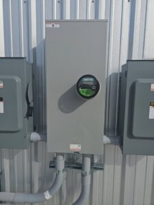 A commercial electrical meter and service panel installed on a corrugated wall by Tesla Alarm and Electrical in Plano, TX