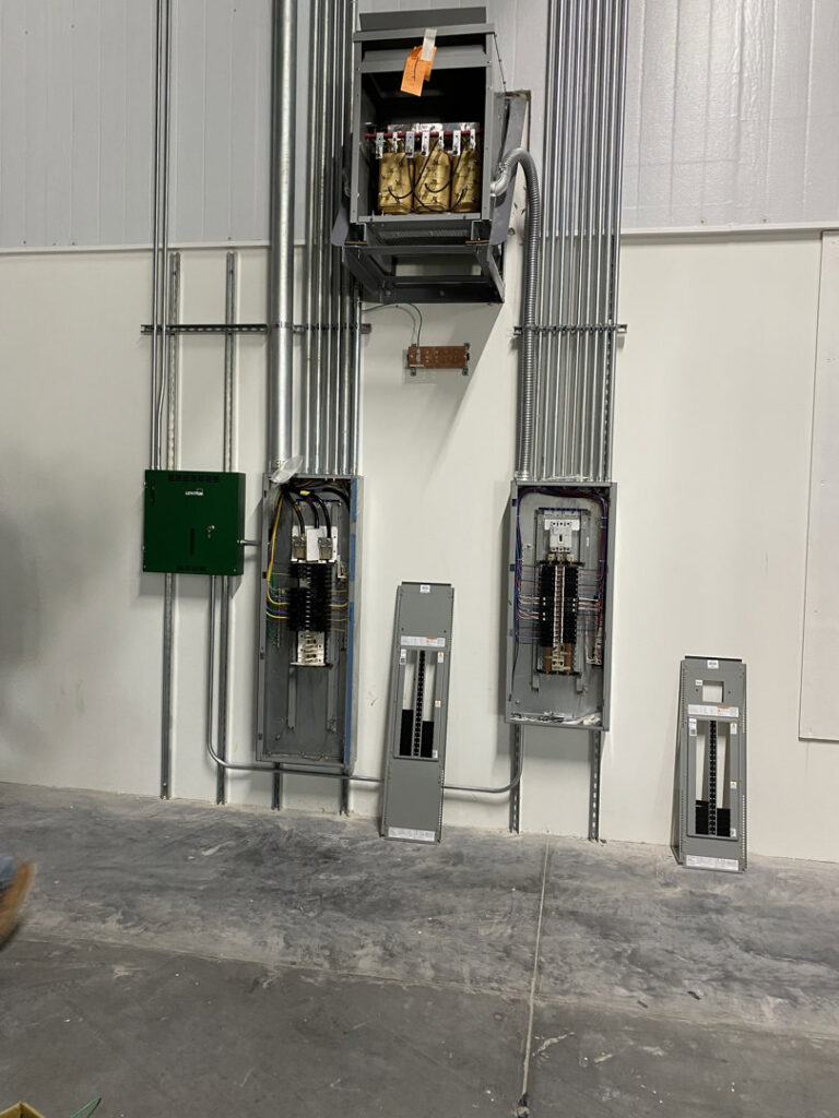 Commercial electrical panels, conduits, and a transformer installed on a wall by Ultralight Electric in Houston, TX.