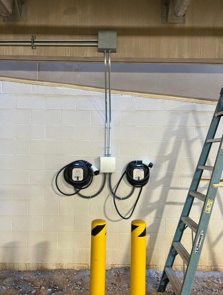 Two commercial EV chargers installed on a white block wall with conduit by Green Volt Electric LLC in Durham, NC.