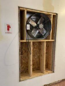 A large commercial exhaust fan being installed in a wall opening by JM HVAC Pros in Elgin, IL.
