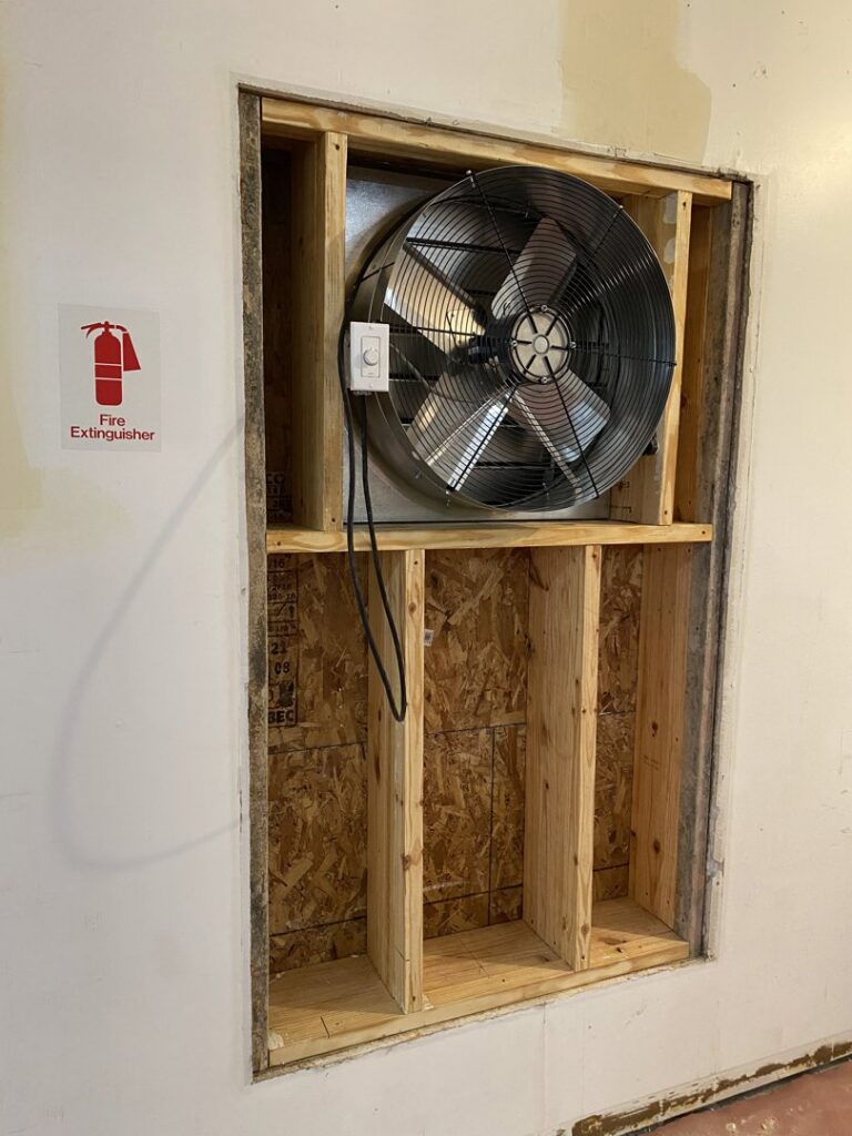 A large commercial exhaust fan being installed in a wall opening by JM HVAC Pros in Elgin, IL.