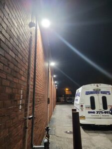 Bright commercial exterior lighting installed on a brick wall at night, with a New York Electrical Design service truck nearby in Freeport, NY