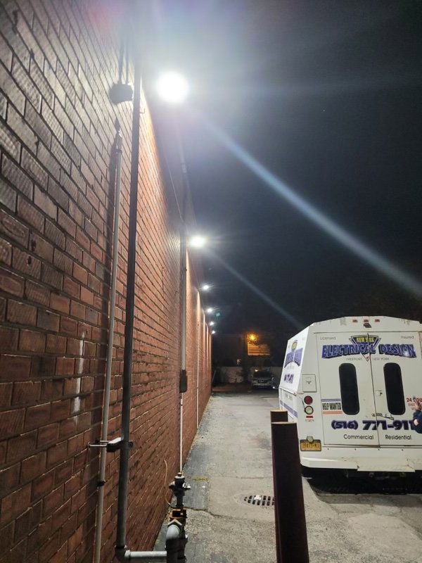 Bright commercial exterior lighting installed on a brick wall at night, with a New York Electrical Design service truck nearby in Freeport, NY