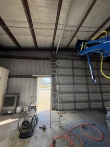 A newly installed white commercial garage door with a ladder nearby, showcasing work by Cajun Doors & More in Lafayette, LA.