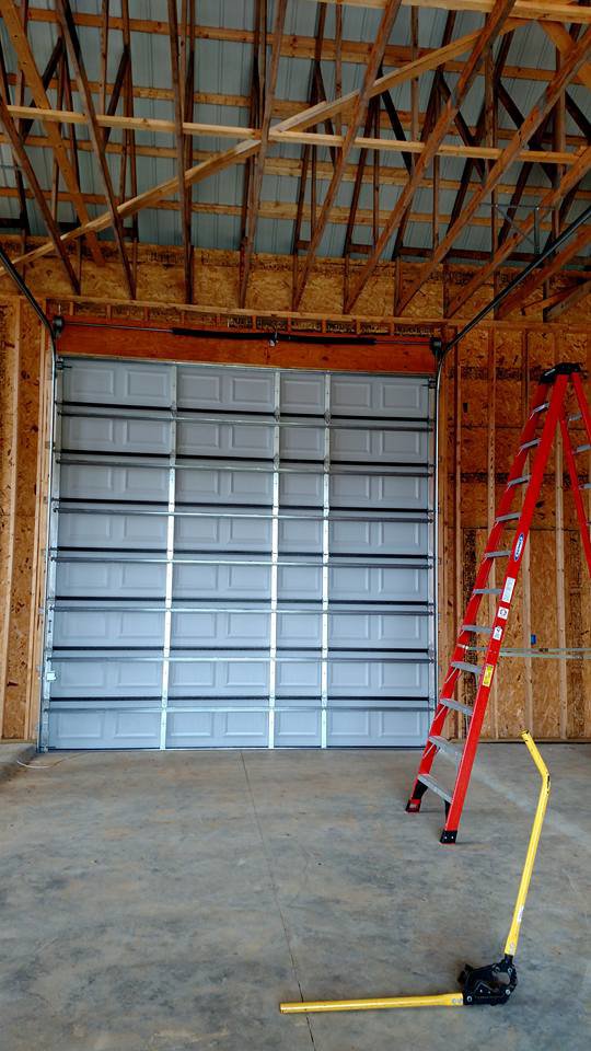Commercial garage door installation in progress with ladders and tools inside a building by Ken's Overhead Door in Clarksville, TN.