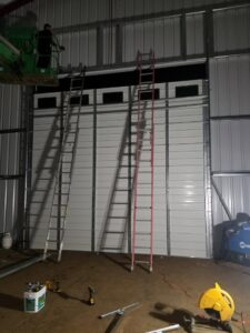 Installation of a large commercial garage door in progress, with ladders and a lift, by Xpress Doors LLC in Salem, OR