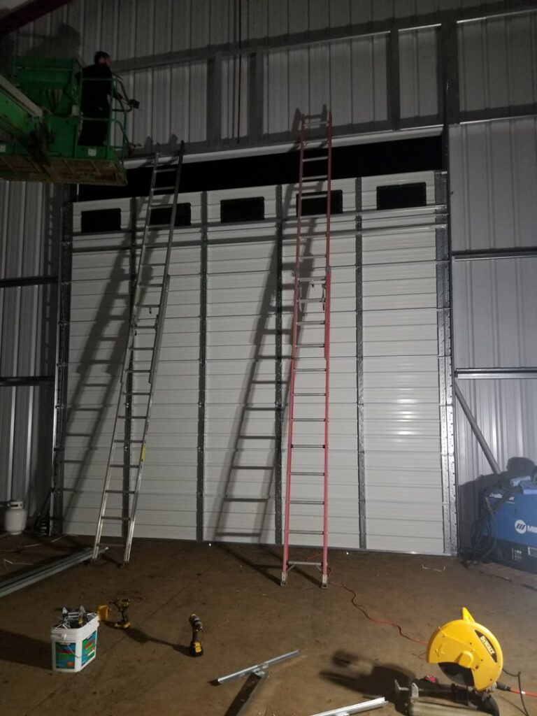 Installation of a large commercial garage door in progress, with ladders and a lift, by Xpress Doors LLC in Salem, OR