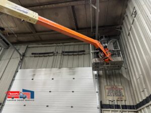 A technician using a lift to perform maintenance on a commercial garage door for QuickFix Garage Door Service in Brighton, MA.