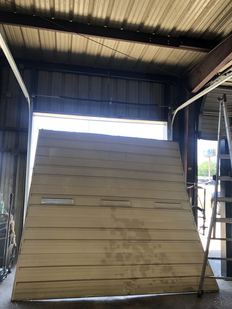 A large commercial garage door panel leaning against the opening, indicating a replacement or repair job by Superior Garage Door & Repairs in Lafayette, LA.