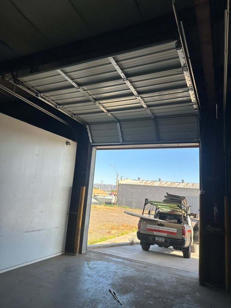 Interior view of a commercial garage door with a service truck outside, indicating a repair or installation job by Central Garage Door Repair LLC in Glendale, AZ.