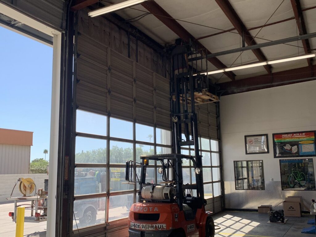 A commercial garage door, partially open, with a forklift inside, serviced by Fix It Now Garage Doors.com in Tempe, AZ.