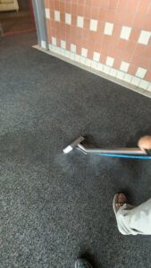 A professional cleaning a commercial hallway carpet with a cleaning wand by Custom Carpet Cleaning in Albuquerque, NM.