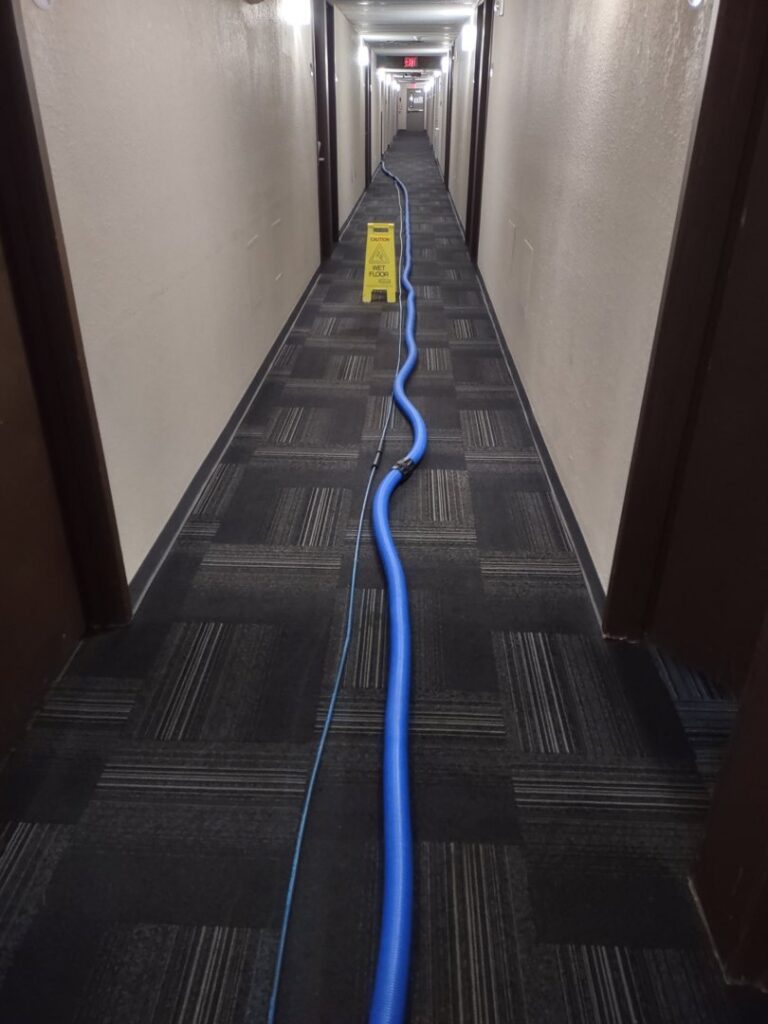 A long commercial hallway carpet being cleaned with equipment hoses by Customer First Carpet Cleaning in Appleton, WI
