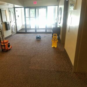 Commercial hallway carpet drying with a fan and wet floor sign after cleaning by Select Carpet Clean LLC in Scranton, PA.