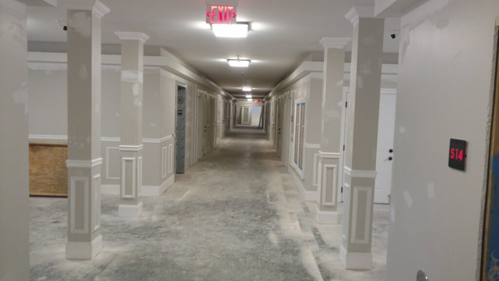 A long commercial hallway under construction, featuring installed ceiling lights and exit signs by Greif Electric Company in Dolgeville, NY.