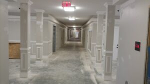 A long commercial hallway under construction, featuring installed ceiling lights and exit signs by Greif Electric Company in Dolgeville, NY.