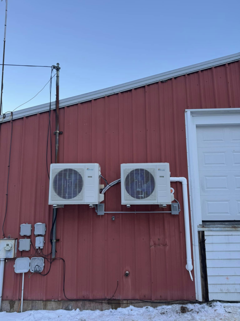 Two heat pump outdoor units installed on the red exterior of a commercial building by S&J Heat Pumps in Augusta, ME.