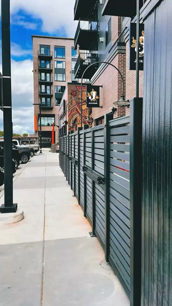 A sleek black commercial horizontal slat fence installed along a sidewalk by Complete Fence, LLC in West Chicago, IL
