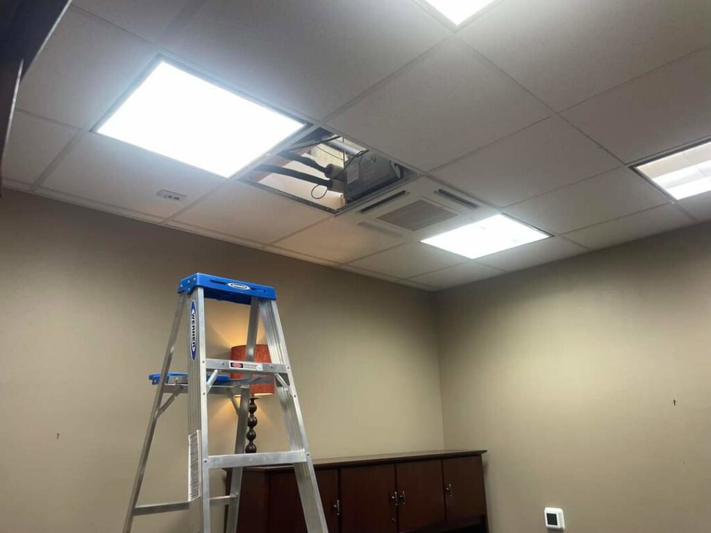 Chapman HVAC servicing a commercial HVAC unit visible through an open ceiling tile in Cleveland, OK.