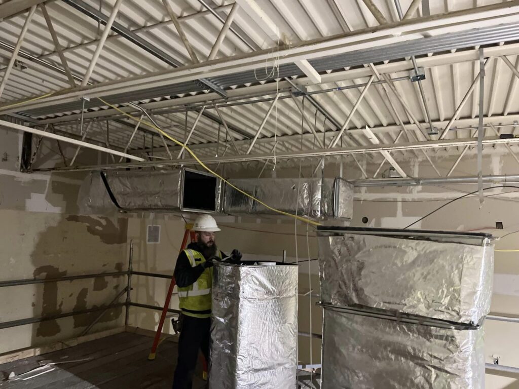 A worker from STAR Heating Cooling Plumbing installing large insulated HVAC ductwork in a commercial building in Fishers, IN.