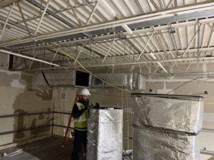 A worker from STAR Heating Cooling Plumbing installing large insulated HVAC ductwork in a commercial building in Fishers, IN.