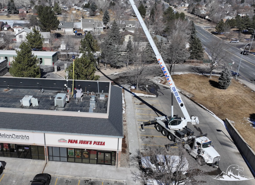 An aerial view of a commercial HVAC unit installation using a crane on a rooftop by Integrity Mechanical Colorado in Denver, CO.