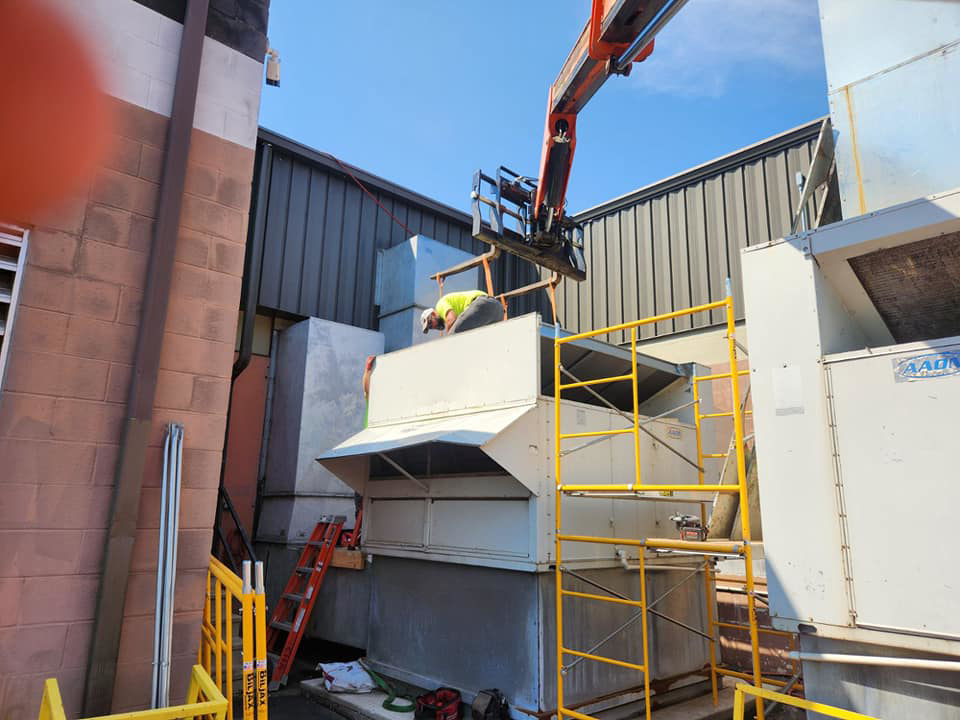 A worker installing a large commercial HVAC unit with a lift and scaffolding for Capitol Heating and Air in Morgantown, PA.