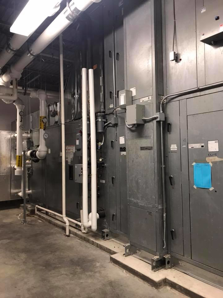 Interior view of a commercial HVAC mechanical room with large air handling units and extensive piping by RTH Mechanical Contractors in Dover, NH.
