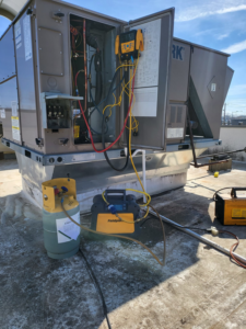 Servicing a commercial rooftop HVAC unit with a refrigerant tank and equipment by Santos Heating and Cooling in St Joseph, MO.