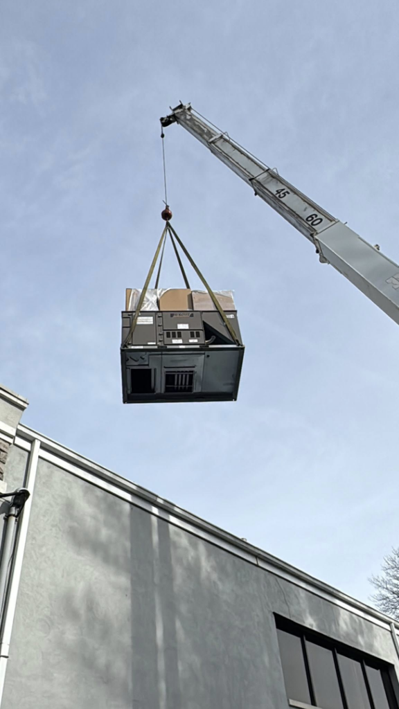 A commercial HVAC unit being hoisted by a crane during a replacement project by Prism Heating & Air Conditioning in Toms River, NJ.