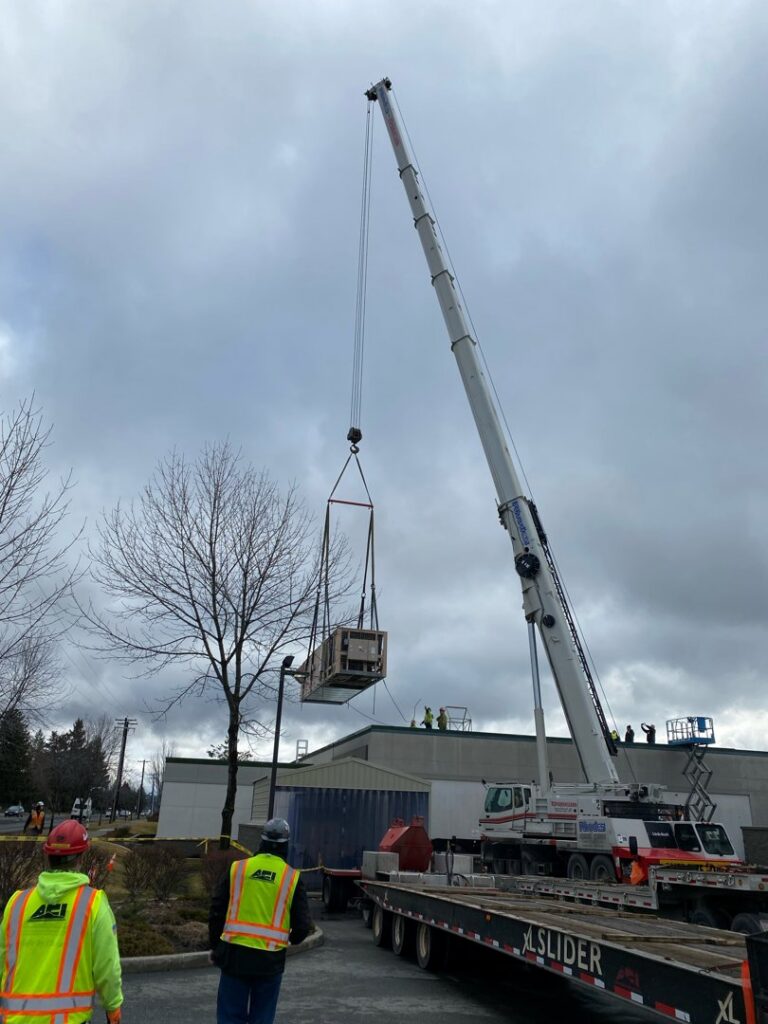 Workers overseeing a crane lifting a commercial HVAC rooftop unit during installation by ACI Northwest Heating, Cooling & Electrical in Dalton Gardens, ID.