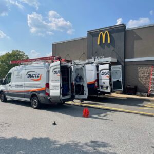 Ductz of Southeast Michigan service vans with open doors and equipment at a commercial HVAC job site in Livonia, MI.