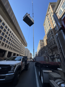 A commercial HVAC unit being lifted by a crane in a city setting for APEX HVAC Solutions LLC in Frederick, MD.