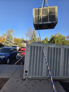 A large commercial HVAC unit being lifted by a crane during installation or removal by High Standard HVAC LLC in Cheyenne, WY.