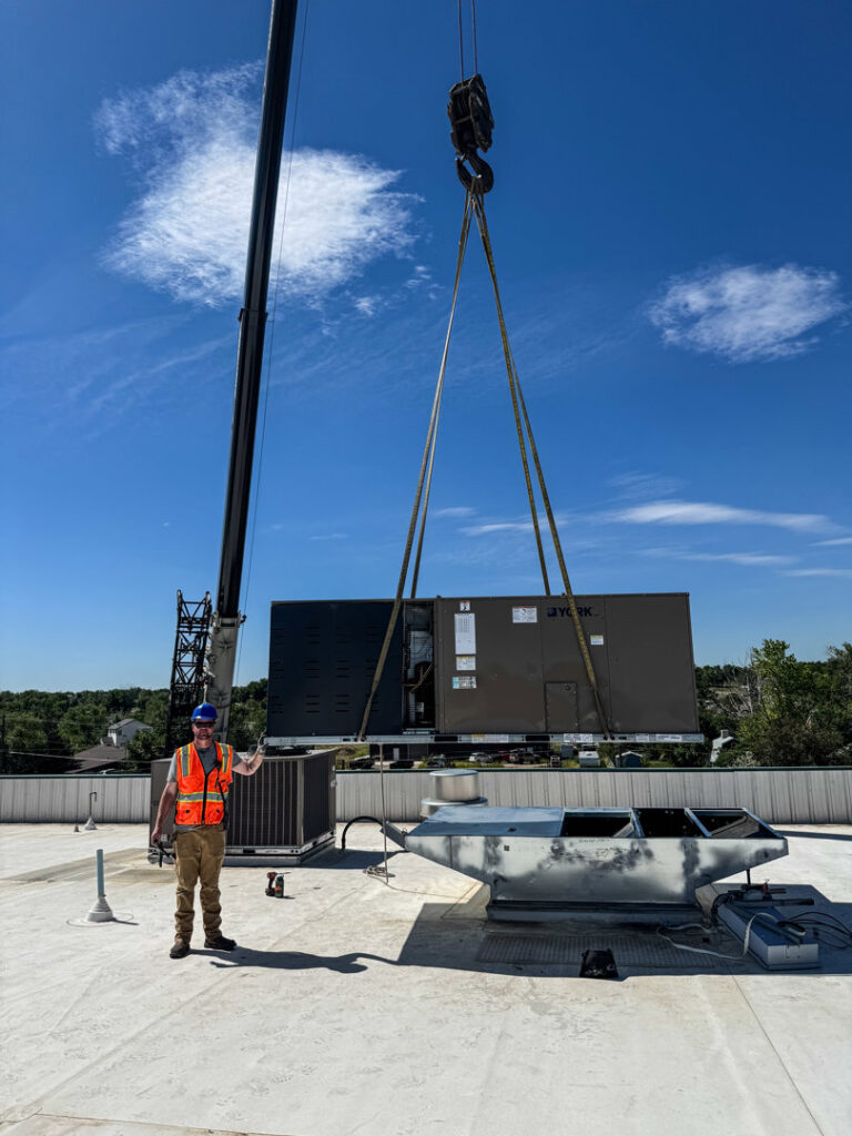 A large commercial HVAC unit being installed by crane on a rooftop by Kraemer Mechanical in Broomfield, CO.