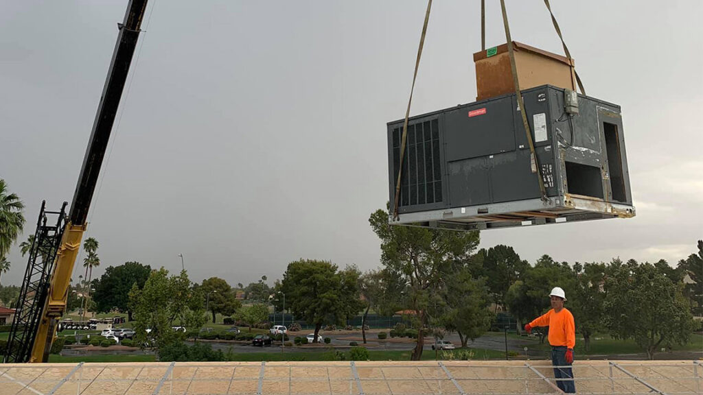 A large commercial HVAC unit being lifted by a crane onto a rooftop for installation by Lincoln Air & Plumbing in Phoenix, AZ