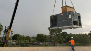 A large commercial HVAC unit being lifted by a crane onto a rooftop for installation by Lincoln Air & Plumbing in Phoenix, AZ