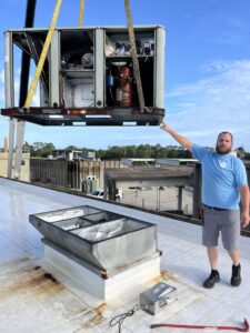 A commercial HVAC unit being lifted by a crane onto a rooftop for installation by McGuffee's Air Conditioning and Heating in Gulfport, MS