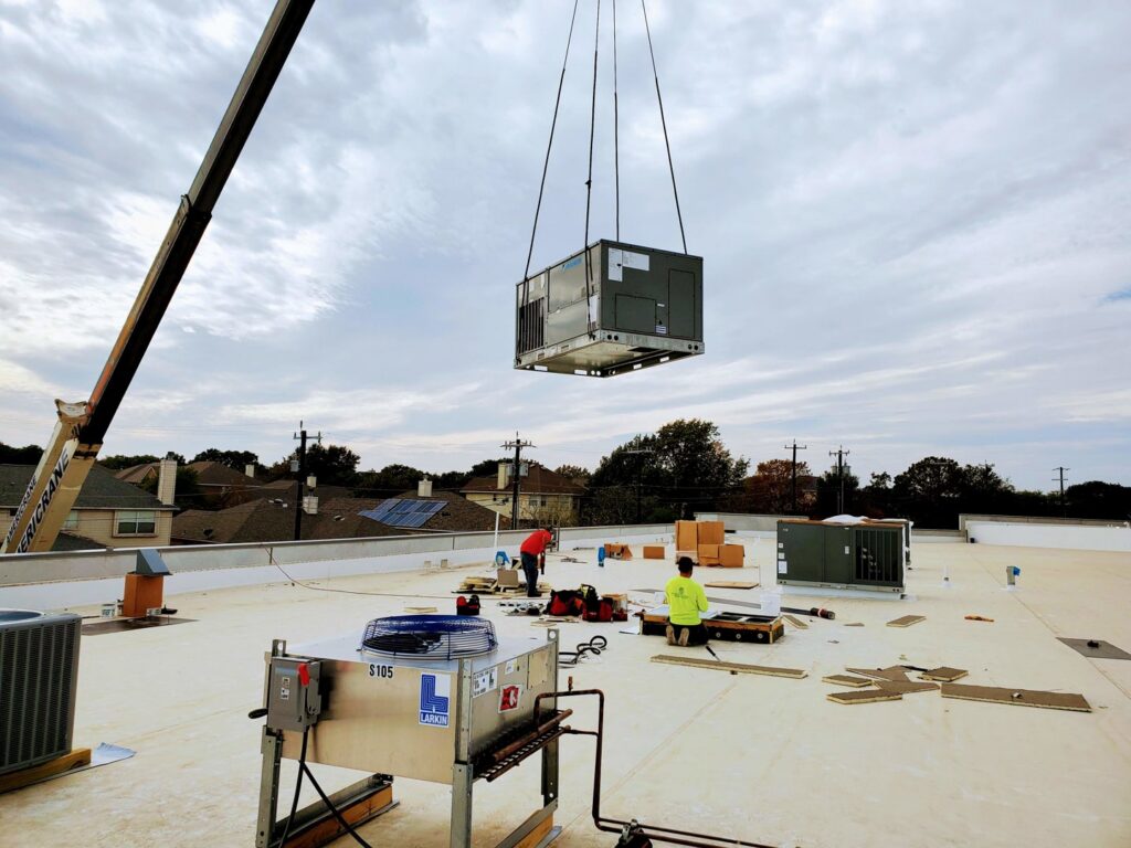 A large commercial HVAC unit being lifted by a crane onto a rooftop by Norway Air Conditioning Inc. in Laredo, TX.
