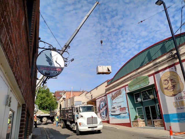 A crane lifting a commercial HVAC unit over a building for installation by Benck Mechanical Inc in Somerset, WI.