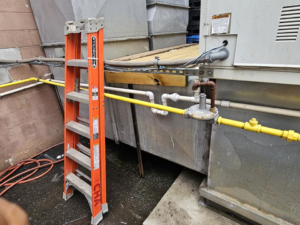 An outdoor commercial HVAC unit with yellow gas lines and an orange ladder, serviced by Capitol Heating and Air in Morgantown, PA.