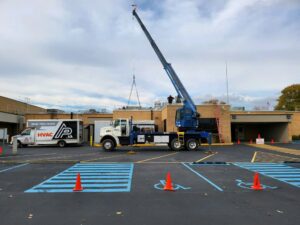 A crane lifting a large commercial HVAC unit onto a rooftop during an installation by AP HVAC in Ridgewood, NY.
