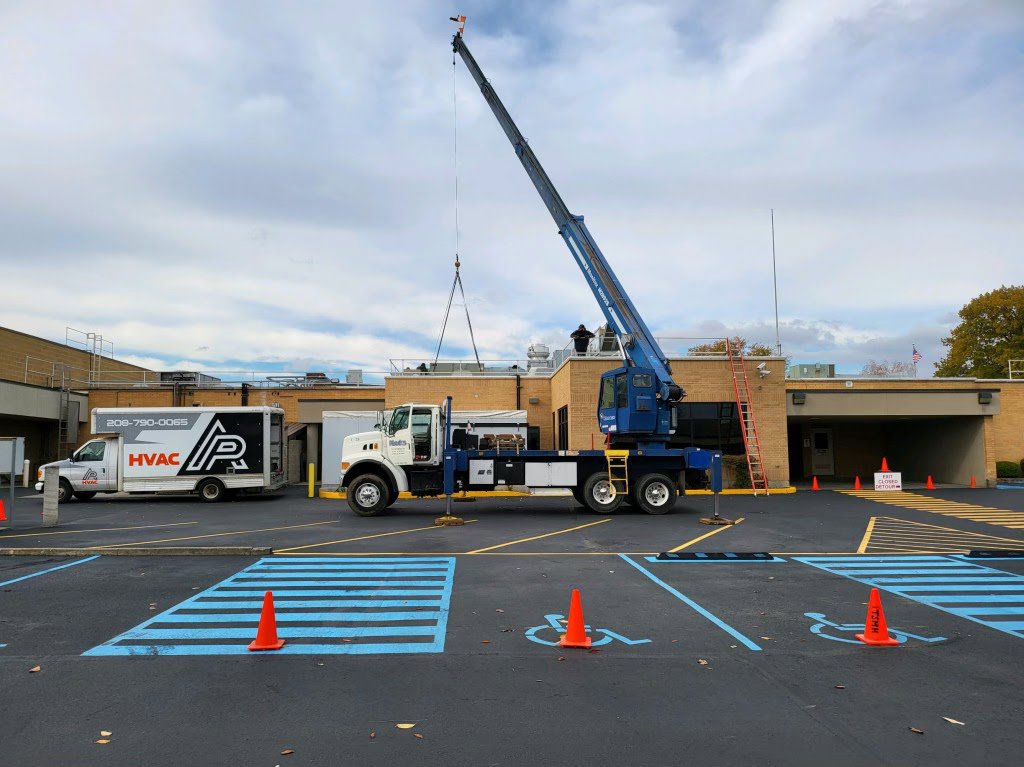 A crane lifting a large commercial HVAC unit onto a rooftop during an installation by AP HVAC in Ridgewood, NY.
