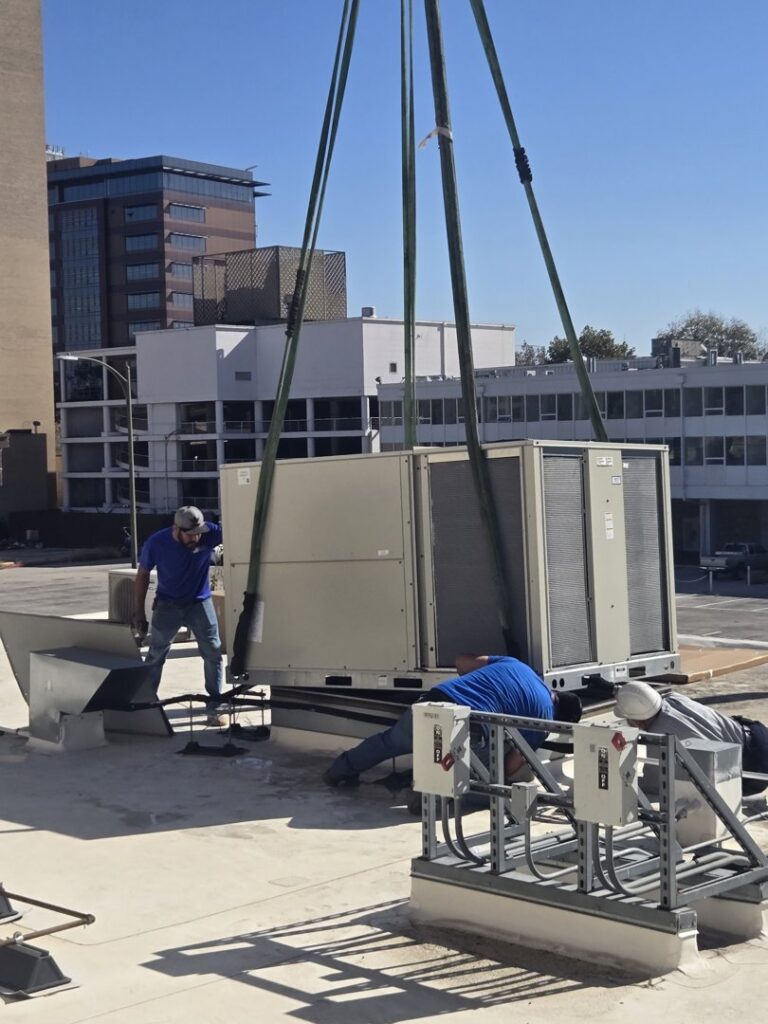 HVAC technicians from Eagle Heating & A/C installing a large commercial unit with a crane on a rooftop in San Antonio, TX.